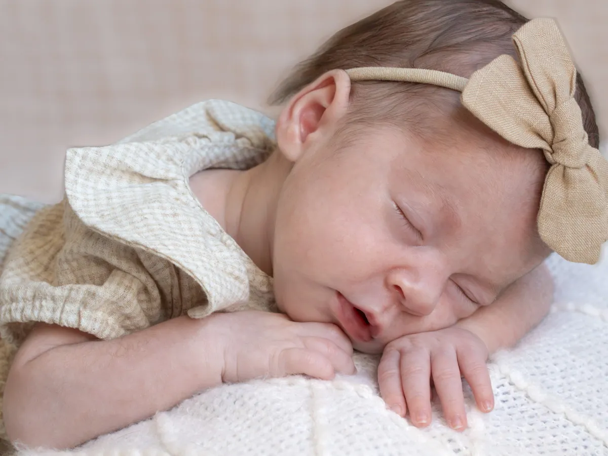 A sleeping newborn in a knitted wrap wearing a linen bow